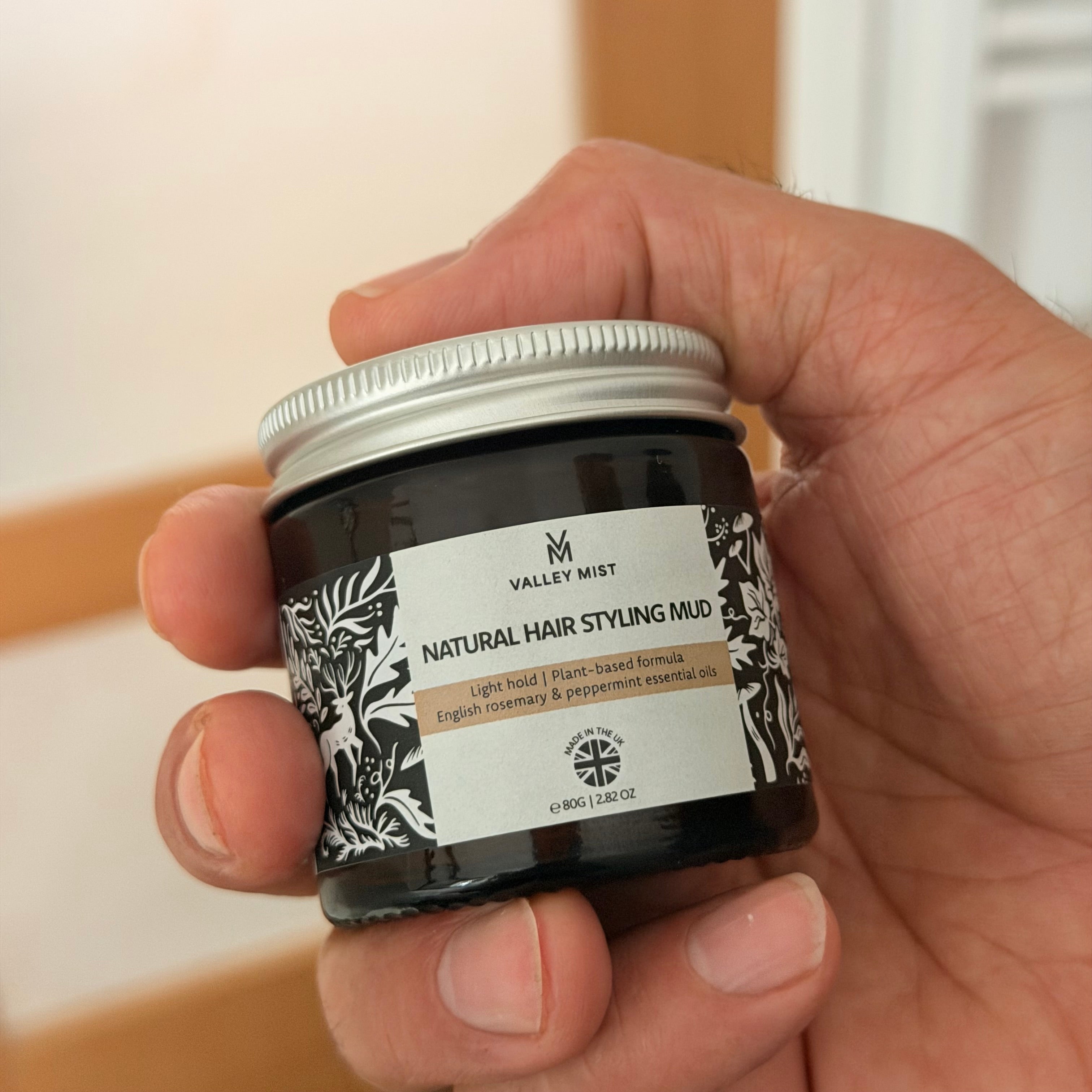 natural hair styling mud in glass jar hand held for size