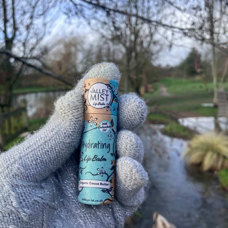 Hand holding Valley Mist hydrating lip balm in biodegradable paper tube to show 10g size