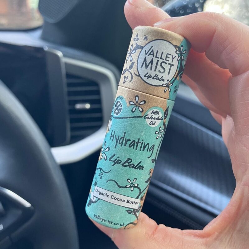 Hand holding Valley Mist hydrating lip balm in biodegradable paper tube to show 10g size